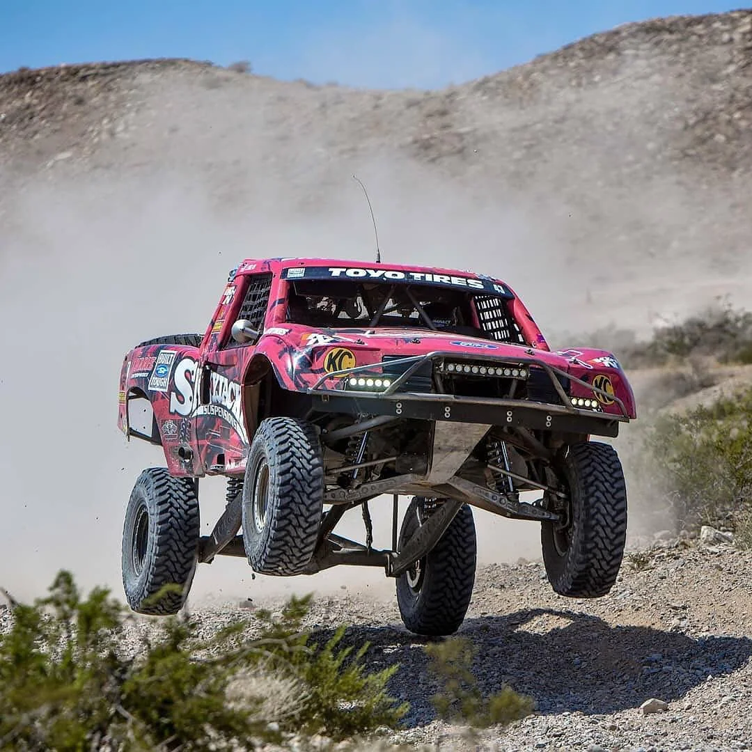 Skyjacker branded red race truck with front wheels airborne during off-road race