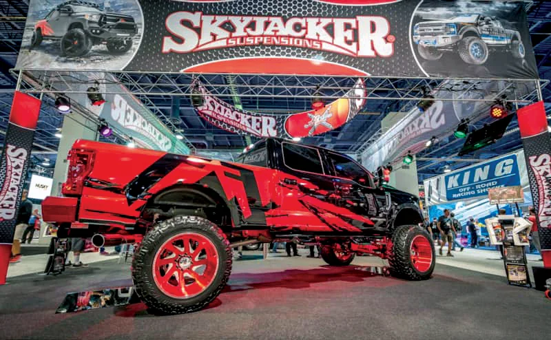 Black and red Skyjacker lifted truck below large hanging banners at SEMA