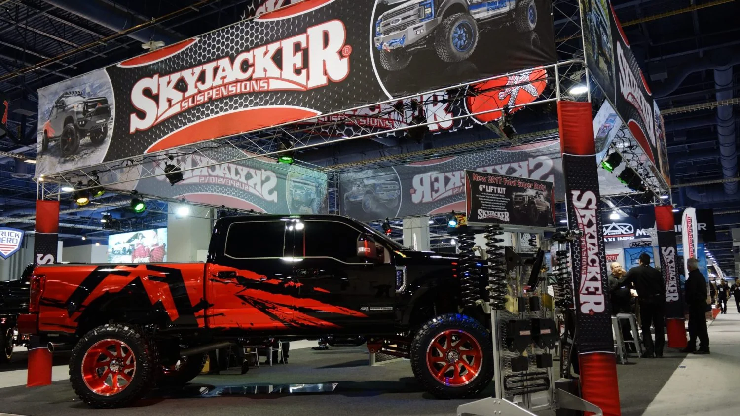 Skyjacker Suspensions SEMA exhibit with overhead branded banners and a black-red lifted Ford truck